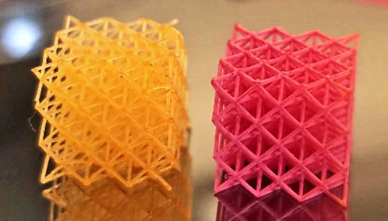 Two 3D-printed cubes have complex lattice work, all covered in yellow and red paint respectively