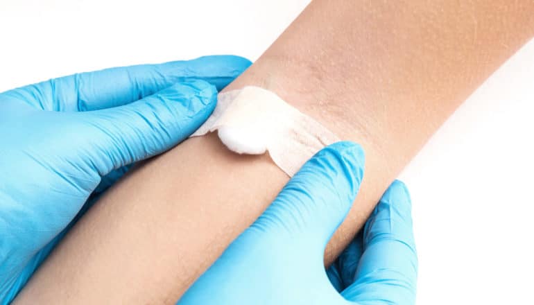 A doctor in blue gloves puts a cotton swab and bandaid on a person's arm after a blood test