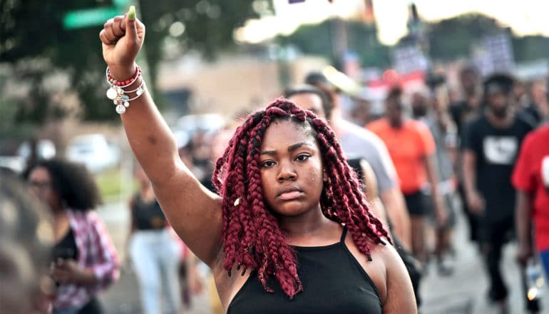 A young woman holds her fist up as she walks with other protestors against police violence