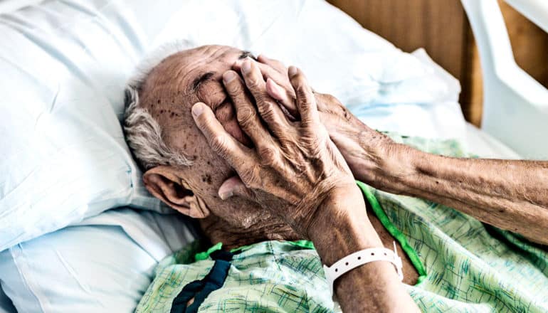 An older hospital patient touches his face while in bed