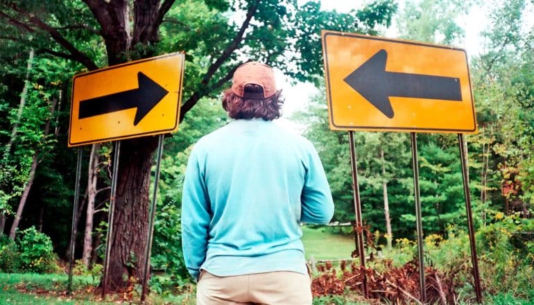 A man stands between two yellow signs pointing in different directions