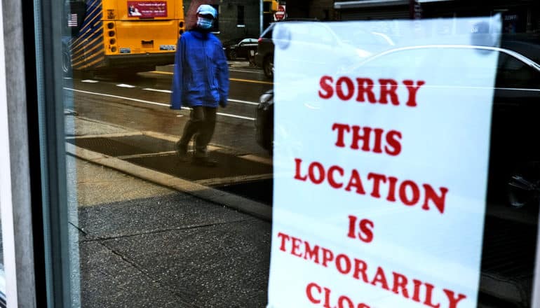 A person in a mask walks past a sign saying "Sorry this location is temporarily closed"