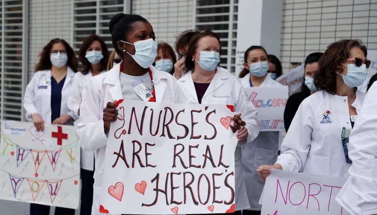 group of nurses wearing masks, one in foreground holds sign saying "nurses are real heroes"