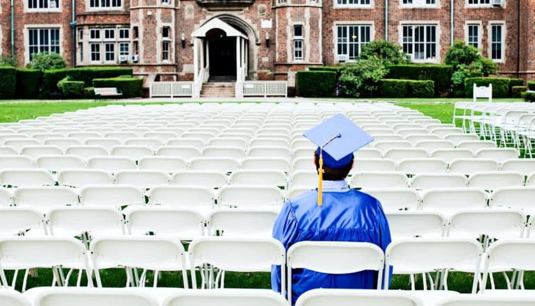 A student sits alone at an empty graduation ceremony in blue cap and gown