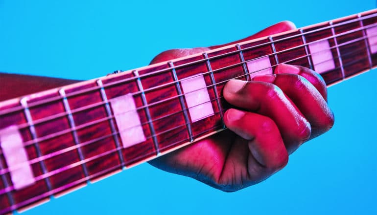 A hand on a guitar fretboard against a blue background