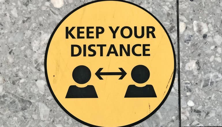 A sign on tile reminds people to "Keep your distance" with an arrow showing space between two figures