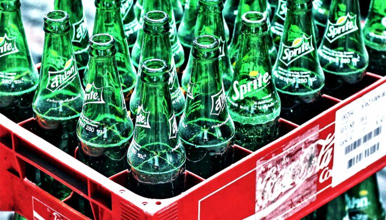 A bunch of green soda bottles sit in a red crate container