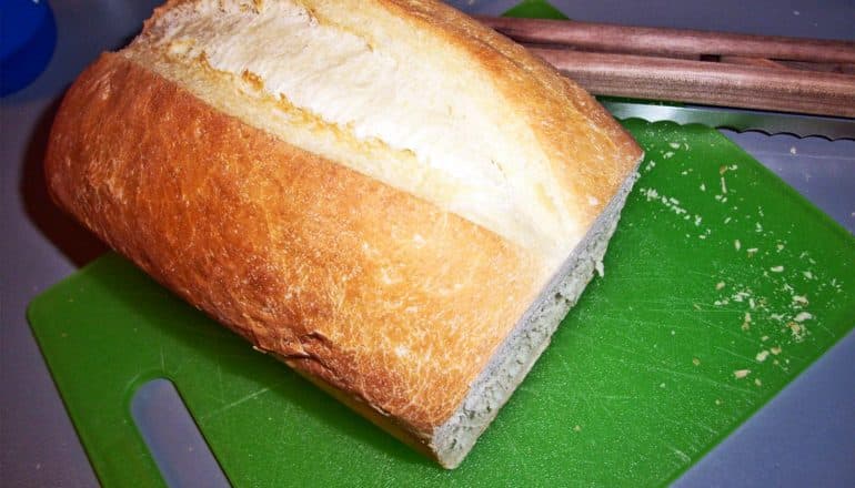 A loaf of sourdough bread sits on a green cutting board