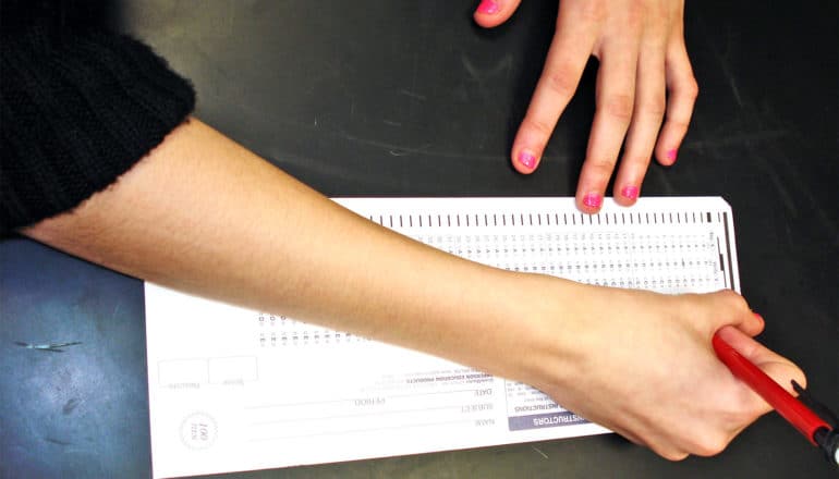 A student fills out a standardized test scantron on a black table