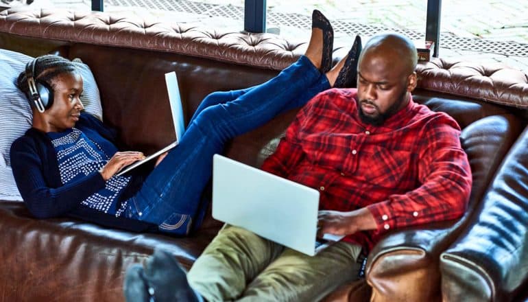 two people use laptops on couch