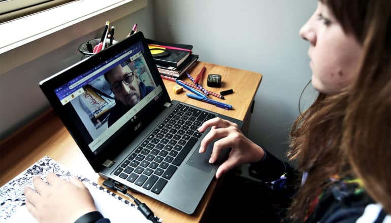 A young student watches her teacher on a laptop