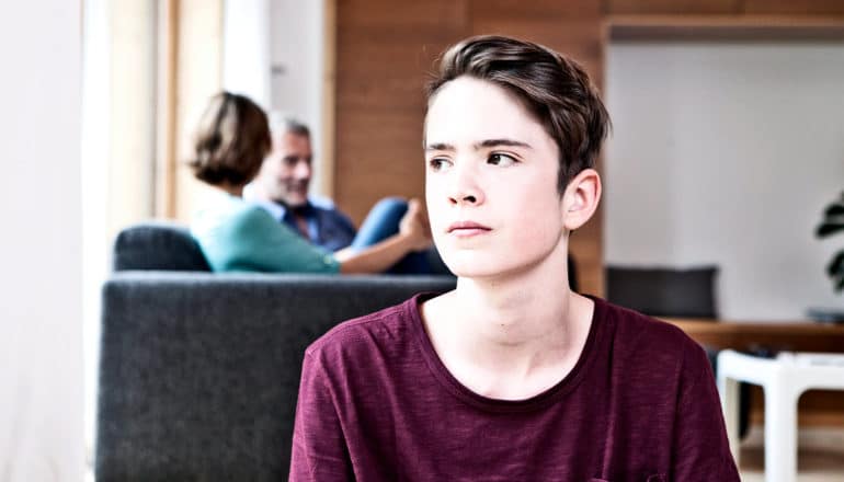 A teen looks off into the distance with his parents in the background