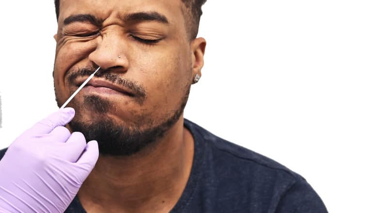 A man winces as a health worker with a purple glove tests him for COVID-19