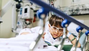 child with glasses reads in hospital bed