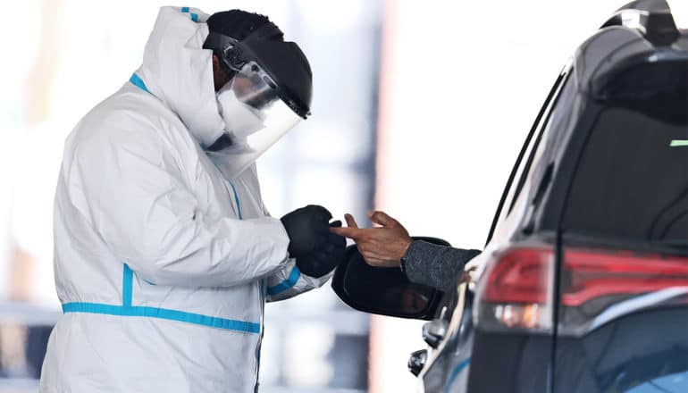 A health worker in white protective gear and a face mask pricks a driver's finger