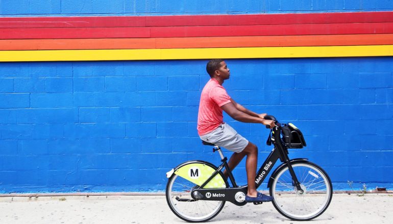 person rides bike share bike along blue wall with rainbow stripe