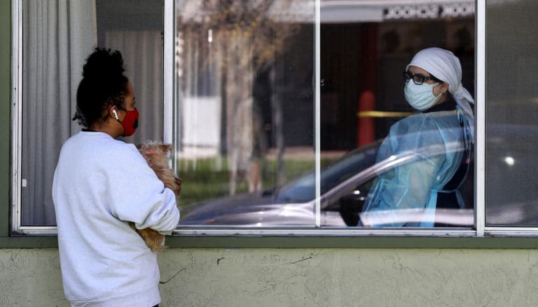 person holds dog outside window talks to health care worker inside