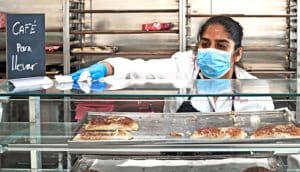 A woman in blue mask and gloves cleans a bakery countertop