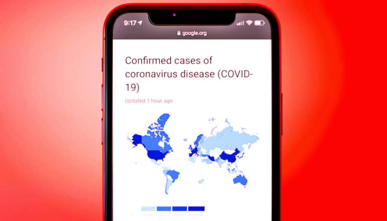 A phone displays a headline about the number of confirmed cases of COVID-19