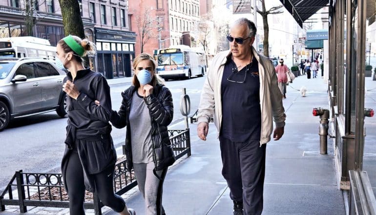 A man without a mask looks at two women in masks as he walks past them on the sidewalk