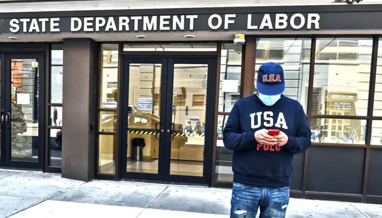 A man in a face mask and a sweatshirt that reads "USA" stands outside a state Department of Labor office building