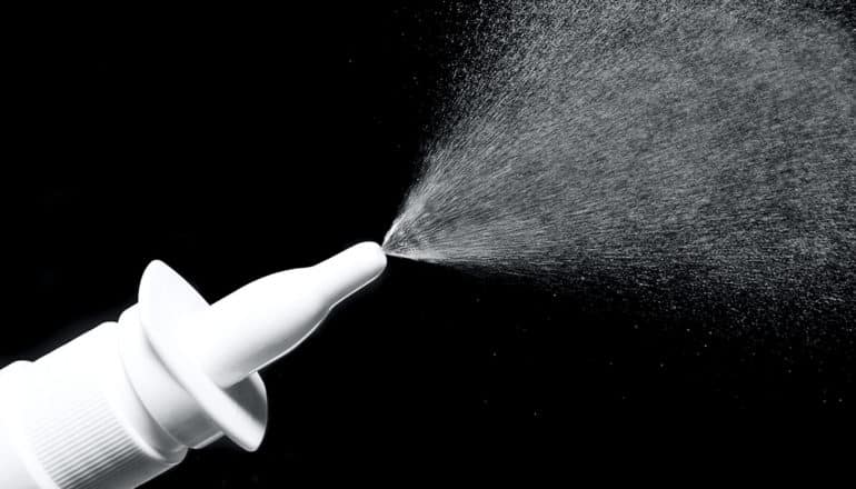 A bottle sprays a fine mist against a black background