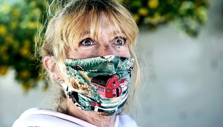 A woman looks scared while wearing a sewn mask with a red barn on it