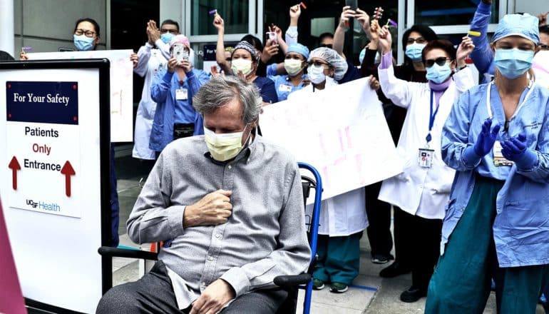 A man leaves the hospital in a wheelchair as nurses and doctors cheer for him