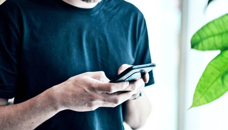 A man in a black t-shirt holds a phone