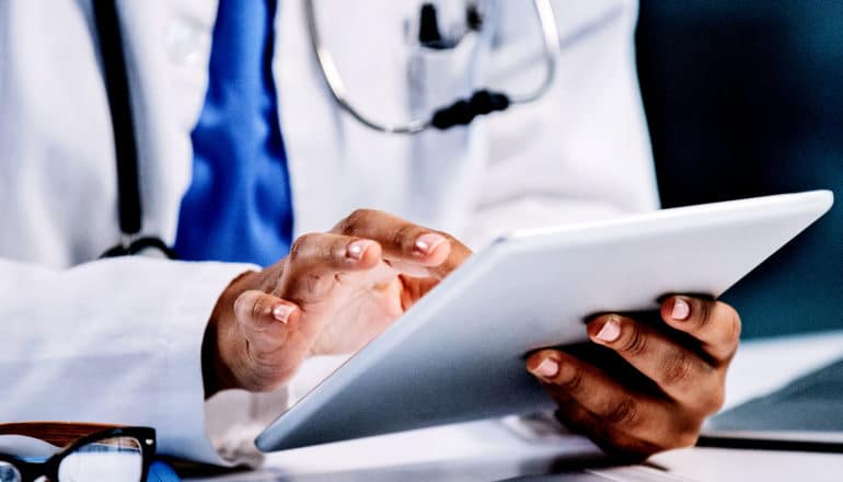 A doctor in a white coat holds a tablet computer