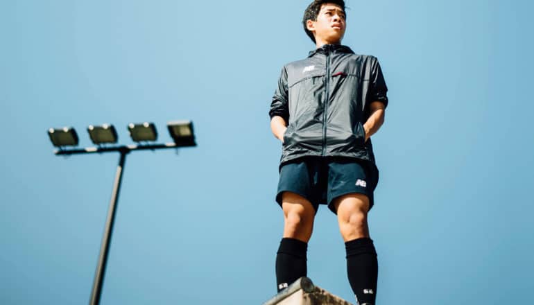 person in tall socks and shorts stands high up with stadium lights behind