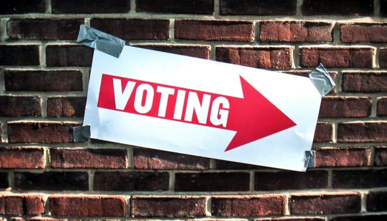 A sign taped to a brick wall reads "Voting" with an arrow pointing right