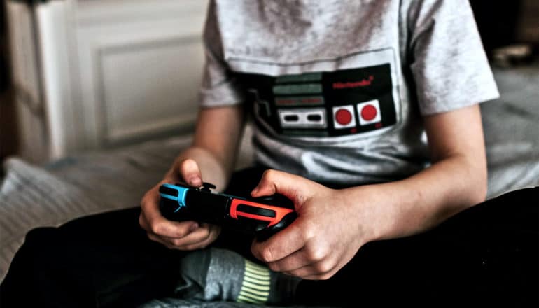 A teen boy plays video games while sitting on his bed