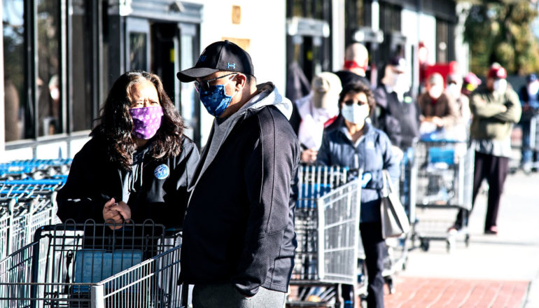 Shoppers stand outside a grocery store wearing masks