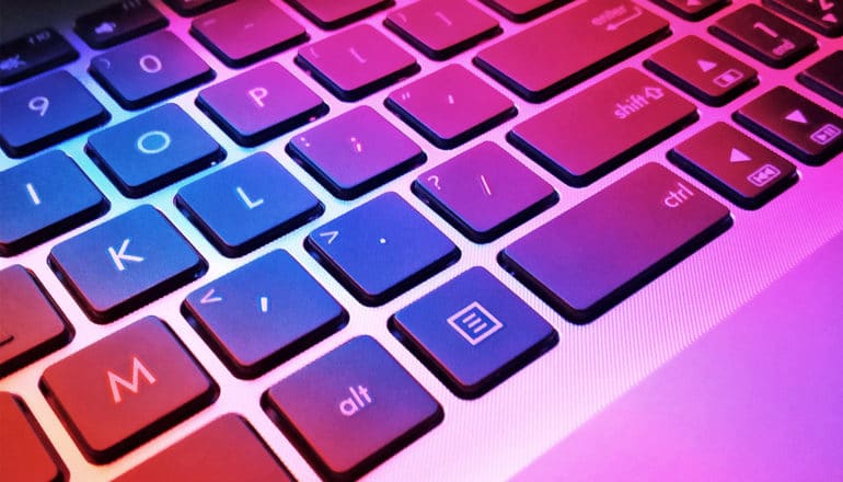 Light from a laptop screen casts pink, purple, and blue light on the keyboard