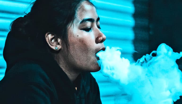 A young woman blows vapor out of her mouth