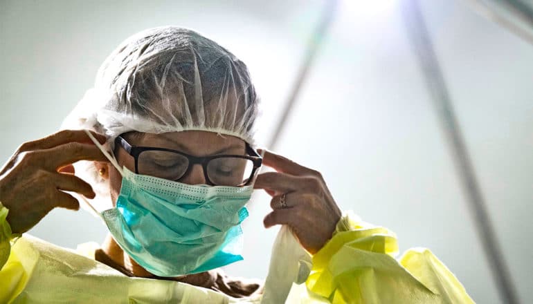 A doctor puts on PPE including a facemask, gown, and cap