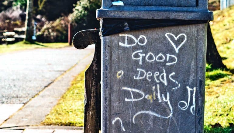 "Do Good Deeds Daily" is written on a trash can next to a bench