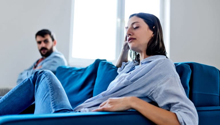 A couple sits on a blue couch arguing