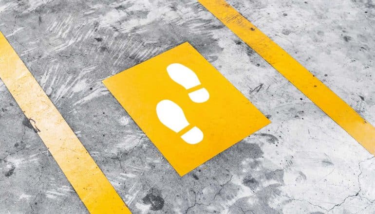 Yellow lines and a yellow square with white shoeprints inside lay diagonally on gray concrete