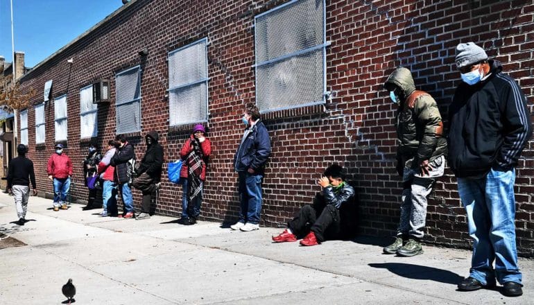 People lean against a brick wall waiting in line for the food bank