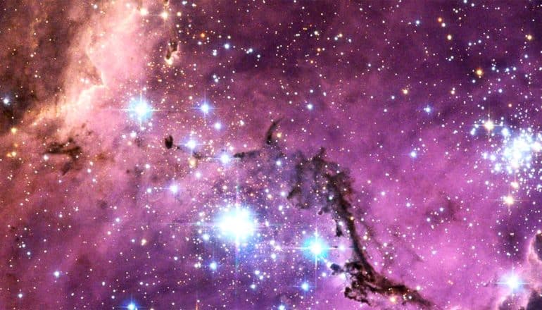 The Large Magellanic Cloud looks purple, with bright white starbursts throughout