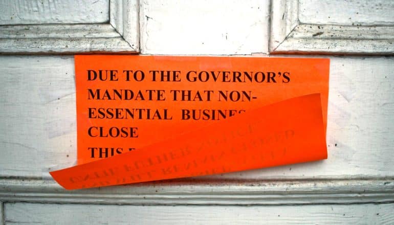 visible part of flapping orange sign on white door says "due to the governor's mandate that non-essential busine- close-"
