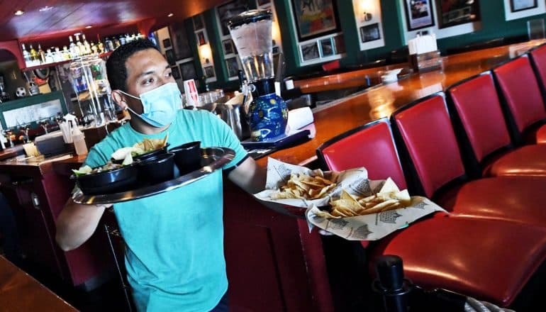 A server carries plates of food to restaurant customers while wearing a medical mask