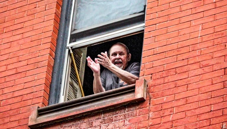 A man looks out his window and seems to shrug at the photographer