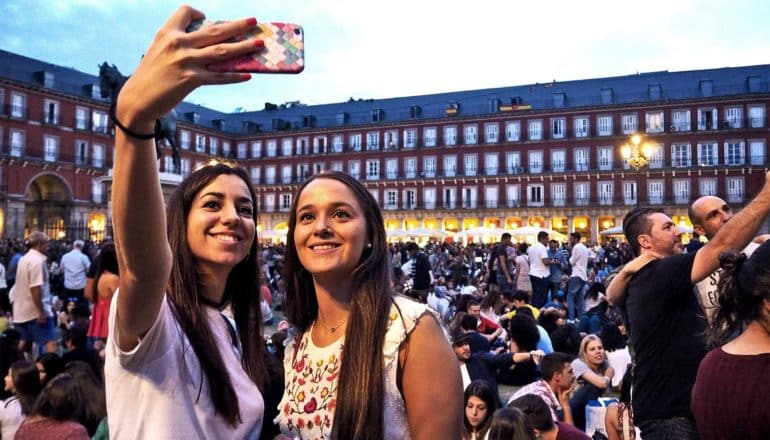 Two young women pose for a selfie in front of a large crowd