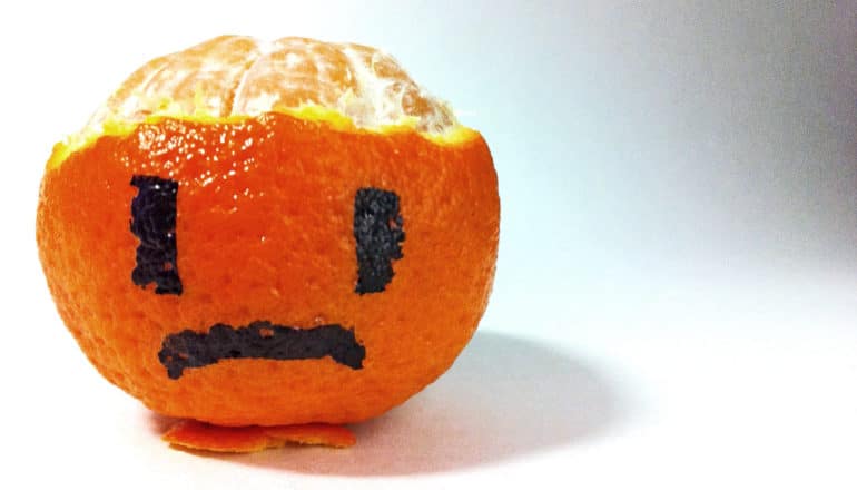 An orange with the top part of the peel off as a frowning face drawn on it