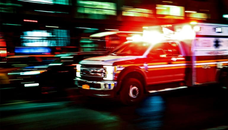 An ambulance with its lights on races through city streets at night