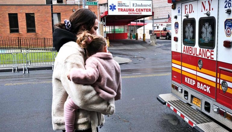 A mother carries her daughter past an ambulance