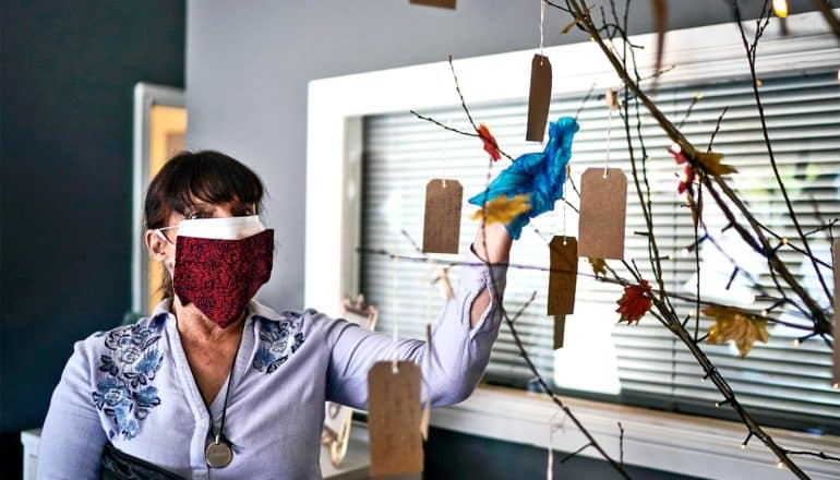 A woman adds a tag to a small tree with many tags hanging off its branches